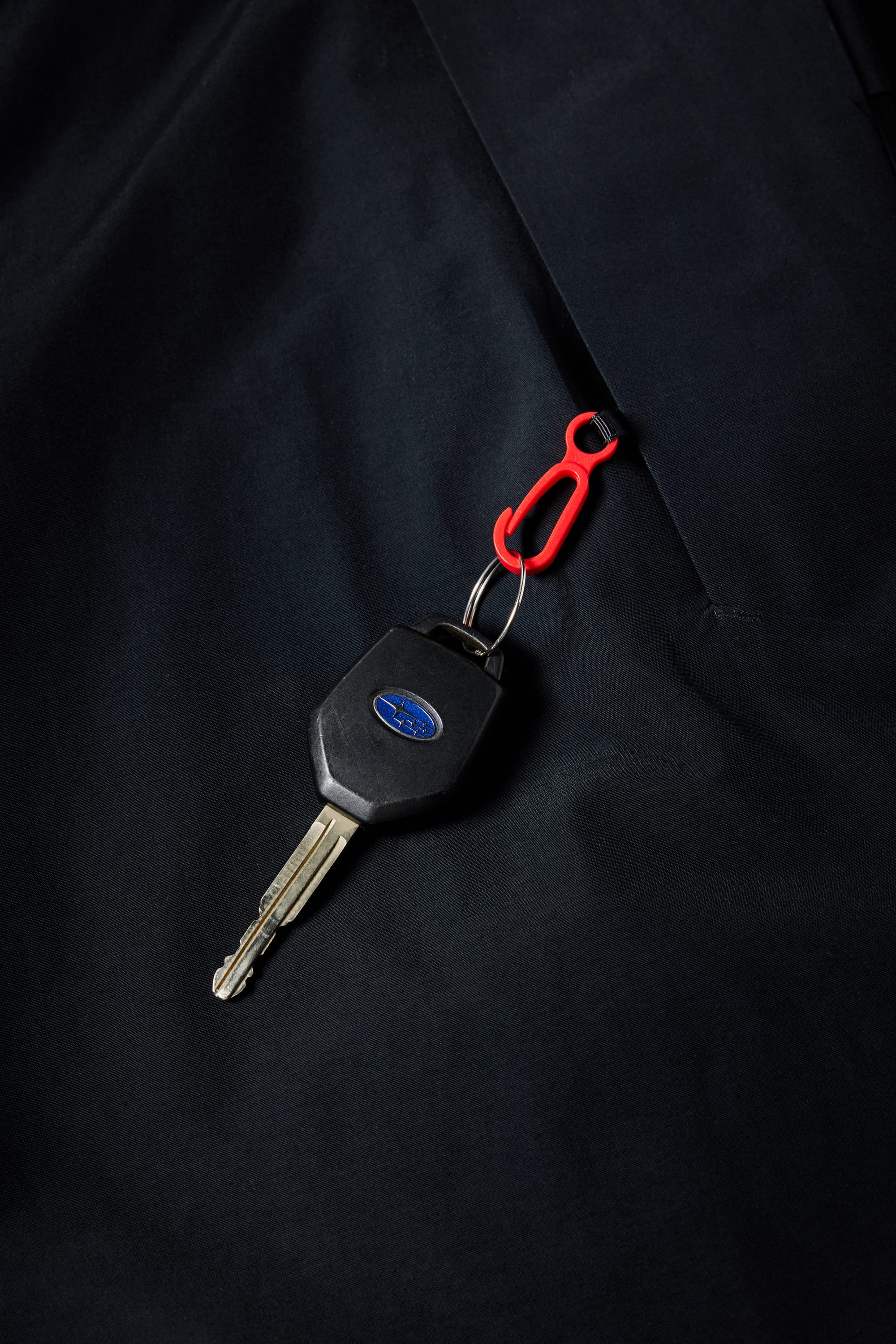 A car key with a blue oval logo and a small red keychain clip rests on the dark, fleece-lined fabric of a 686 Mens Waterproof Hoody by 686.