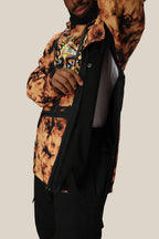 A person wearing the 686 Mens Waterproof Hoody in tie-dye orange and black with a graphic tee lifts one arm, revealing a side zipper and black fleece lining. The plain, light background highlights the 686 brand hoody’s features.