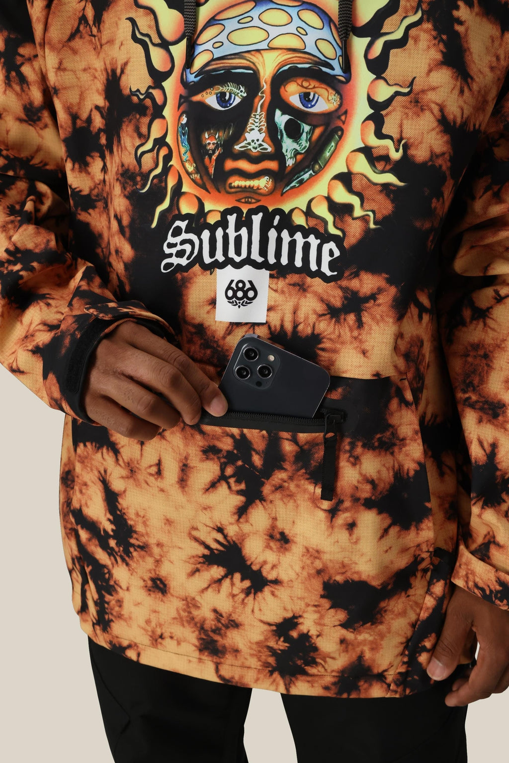 A person wearing the 686 Mens Waterproof Hoody with fleece lining and a colorful sun face design places a smartphone into its front zippered pocket.