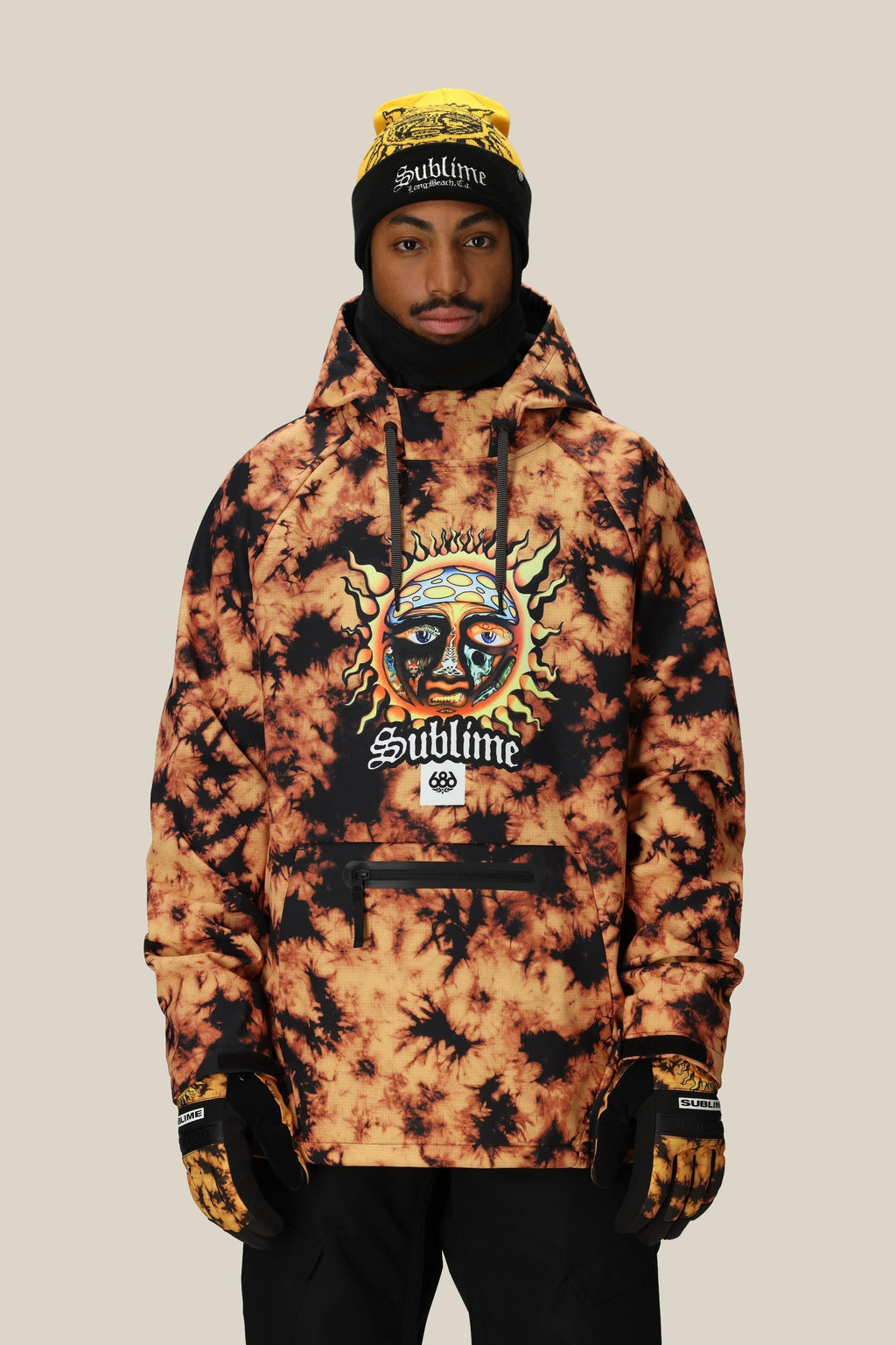 A person wearing a yellow and black 686 Mens Waterproof Hoody by 686, along with black gloves, a black ski mask, and a yellow Sublime beanie, stands against a plain beige background.