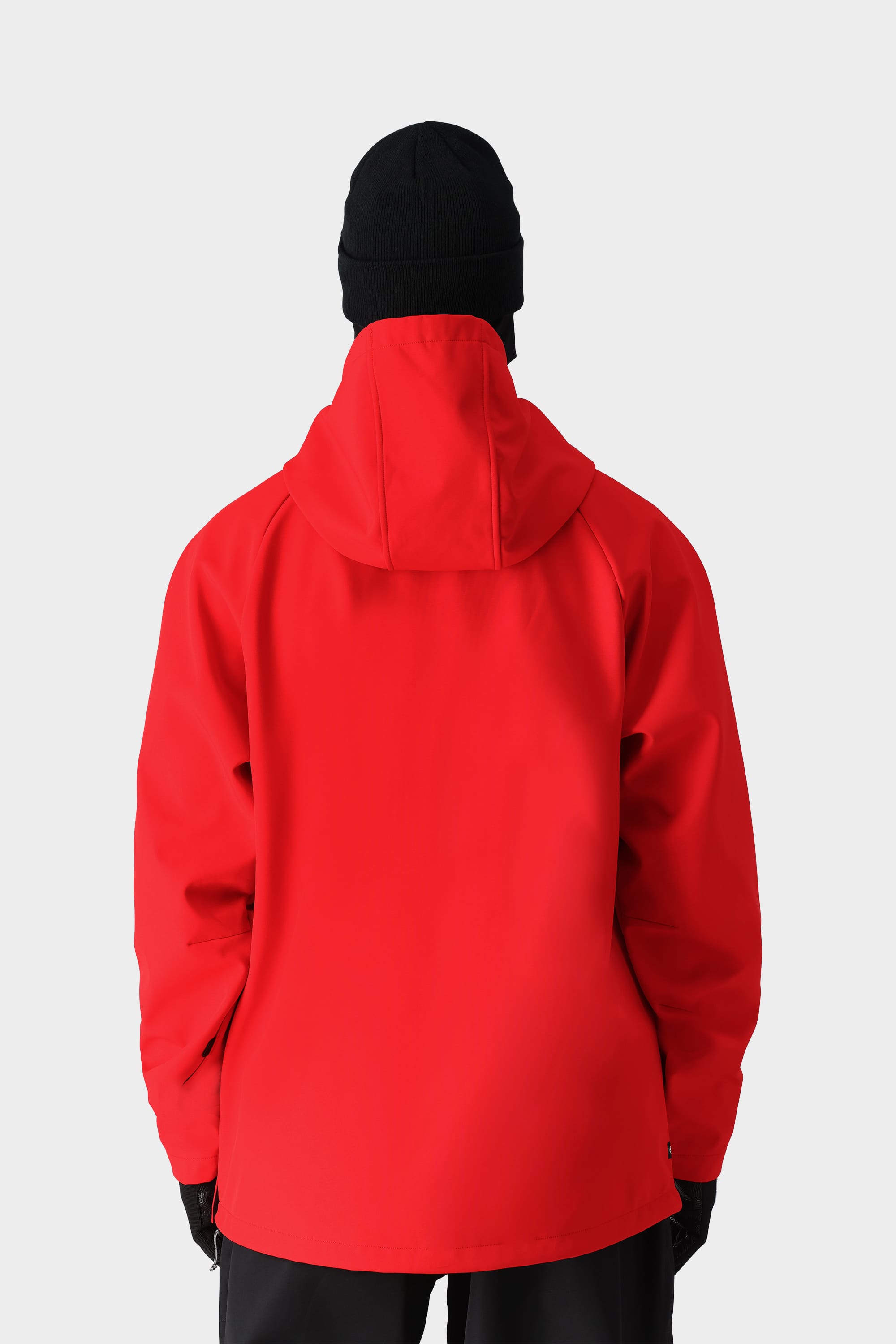 A person wearing the 686 Mens Waterproof Hoody in bright red, paired with a black beanie, black gloves, and black pants, stands with their back to the camera against a plain light gray background.