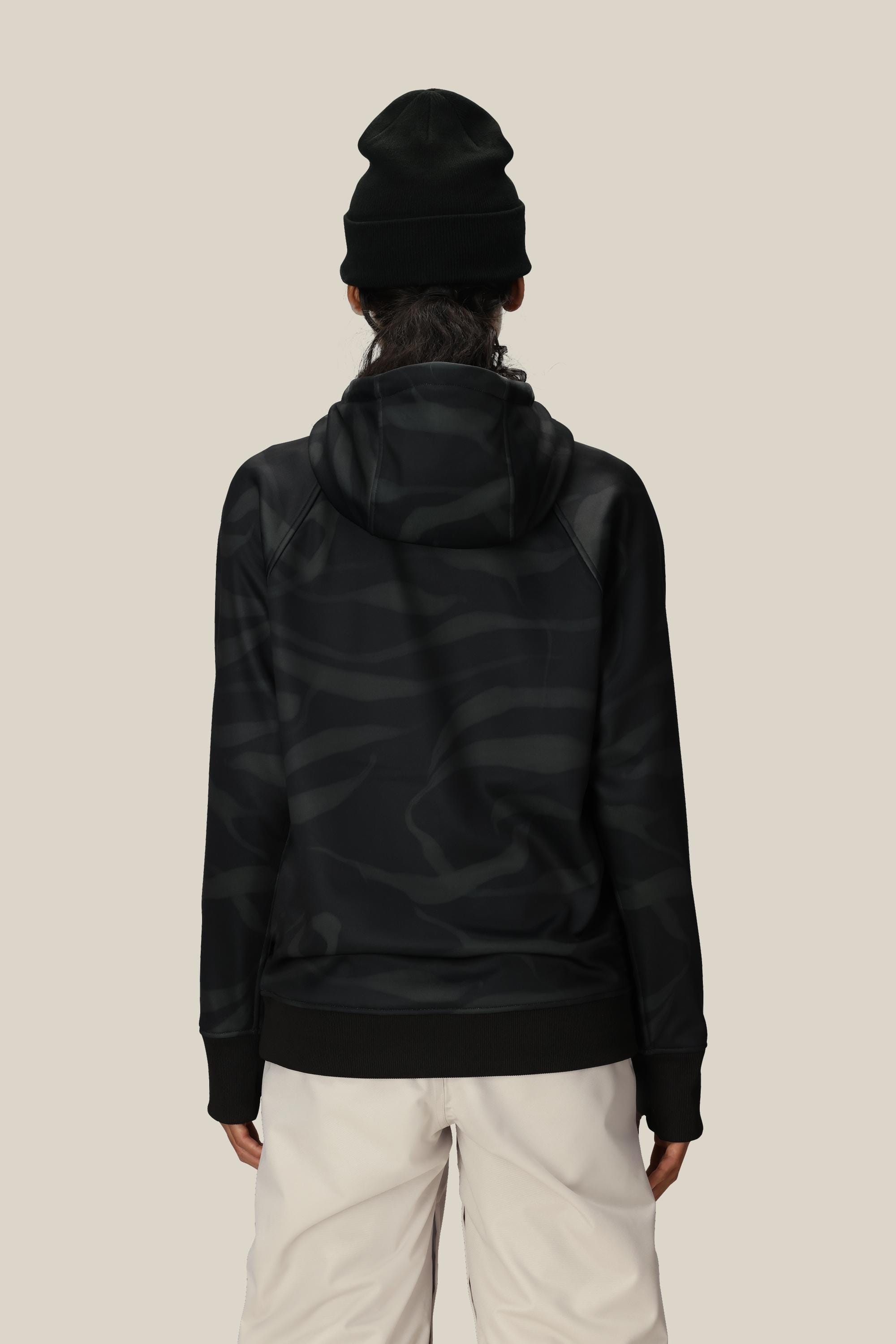 A person wearing a black beanie, light-colored pants, and the 686 Womens Bonded Fleece Pullover Hoody by 686 stands facing away against a plain beige background.