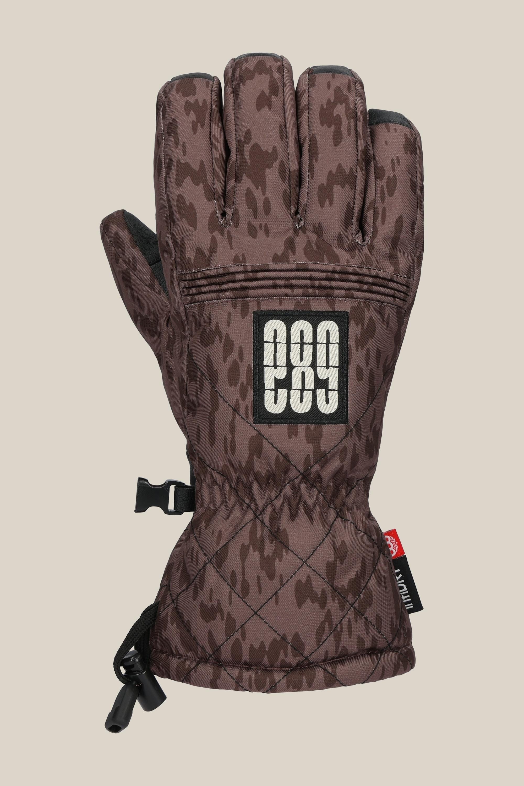 The 686 Women's Jubilee™ Glove features a brown camo pattern with black accents, adjustable wrist strap, a rectangular patch with white "686," plus a black clip and drawstring for convenience.