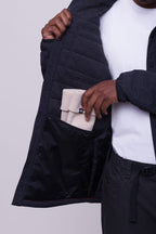 A person in a white 686 Men's Thermaldry™ Snap-Up Shirt opens a black jacket to reveal its inner pocket, where they place a folded beige merino blend knit hat—ideal for stylish citywear.