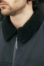 Close-up of a man in the 686 Mens Caim Insulated Jacket, featuring a textured black sherpa collar and front zipper. His face is partially visible, with a trimmed beard and short brown hair.