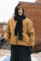 A person wearing the 686 Mens Caim Insulated Jacket stands outside in front of a brick building on a cold day, paired with a black scarf and black gloves.