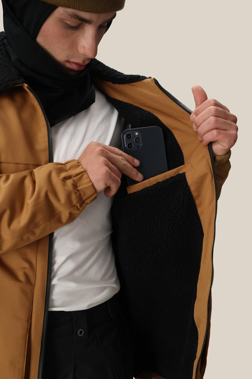 A person in the 686 Mens Caim Insulated Jacket unzips it to place a smartphone in the black fleece-lined inner pocket, with easy access and warmth provided by the cozy 686 jacket.