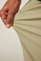 A hand stretches the olive-green 686 Men's Everywhere® Ripstop Short, highlighting the durable stretch ripstop fabric and subtle checkered texture from 686.