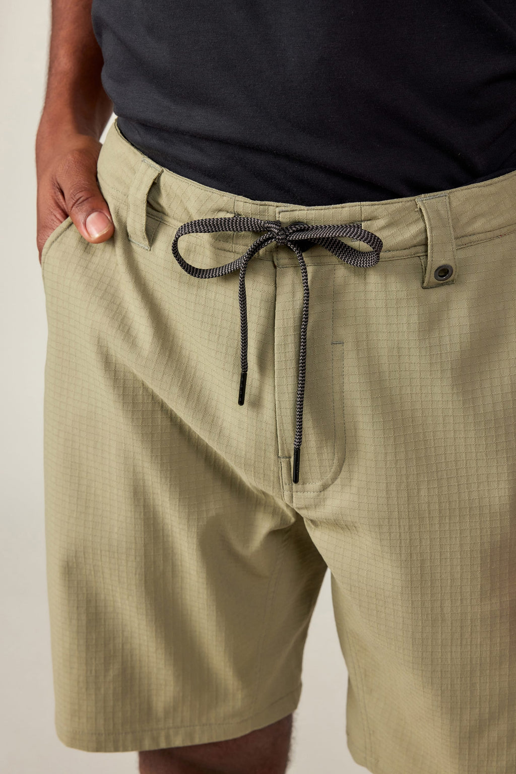 Someone wearing 686 Men's Everywhere® Ripstop Short in light khaki with a black and white drawstring, paired with a black shirt and one hand in their pocket.