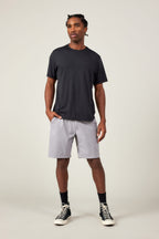 A man stands against a plain background wearing a dark t-shirt, 686 Men's Everywhere® Ripstop Short by 686, black crew socks, and black high-top sneakers. He has one hand in his pocket and looks slightly to the side.