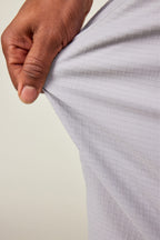 A hand stretches the light gray, durable 686 Men's Everywhere® Ripstop Short fabric, showing its flexibility and subtle grid pattern—perfect for 9-inch shorts. The neutral background keeps the focus on the stretch material from 686.