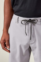 A person wearing 686 Men's Everywhere® Ripstop Shorts in light gray with a black-and-white drawstring by 686, paired with a black shirt, shown from the waist down with one hand visible at their side.