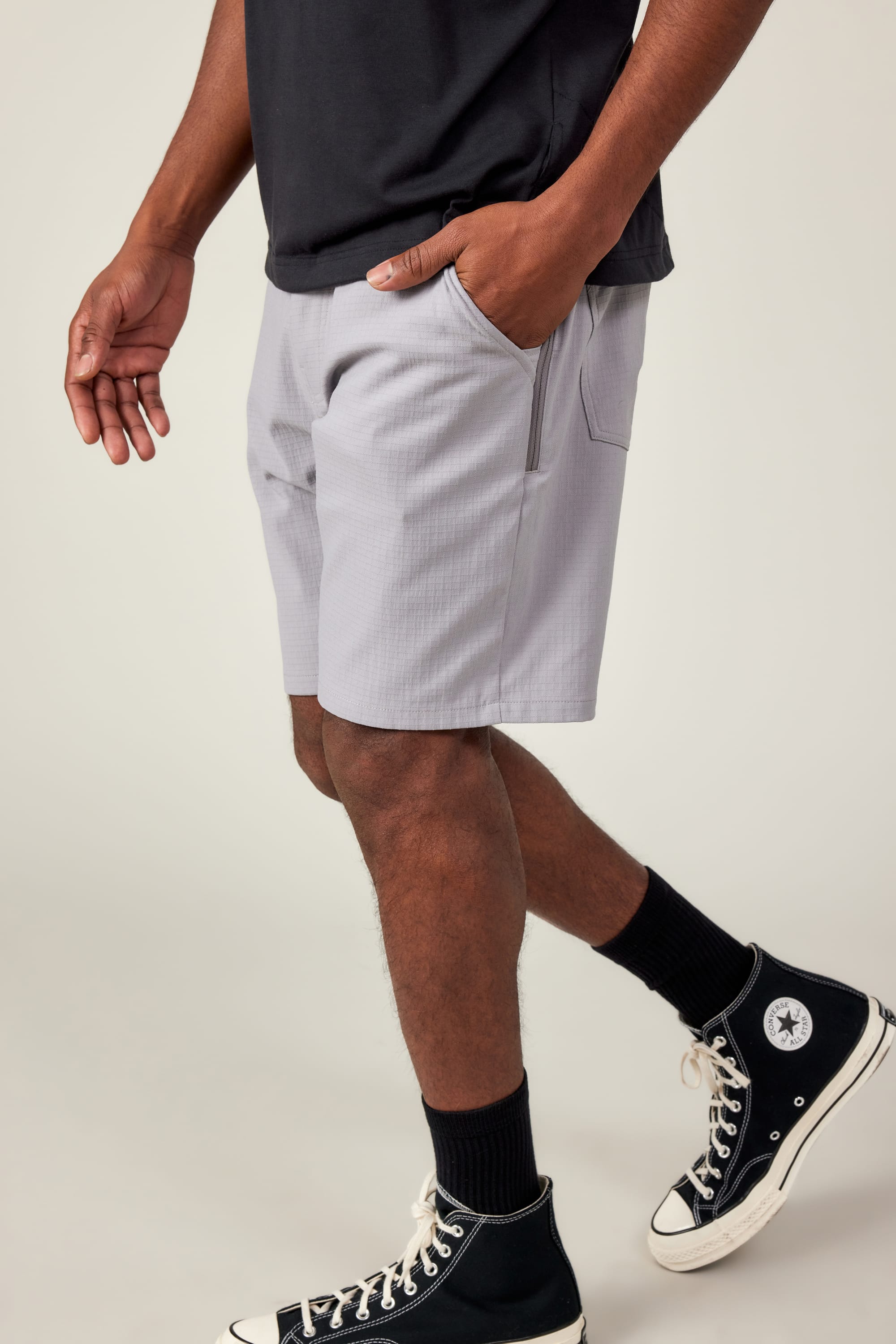 Someone wearing a black t-shirt, 686 Men's Everywhere® Ripstop Short in light gray, black socks, and black Converse sneakers stands with one hand in their pocket against a plain background.