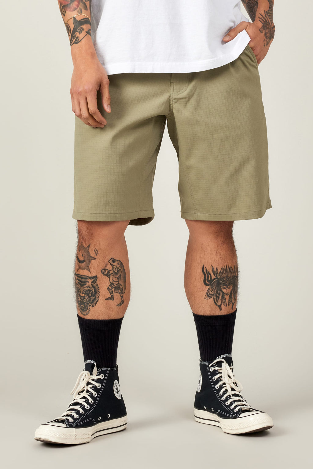 A person wears 686 Men's Everywhere® Ripstop Short - Relaxed Fit in olive green, a white T-shirt, black crew socks, and black high-top Converse. Their tattooed legs and hands rest by their sides against a plain light gray background.