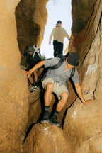 Outfitted in 686 Men's Everywhere® Ripstop Short - Relaxed Fit, three hikers carefully navigate a narrow, rocky passageway with steep walls, moving cautiously between the rocks and ready for adventure.