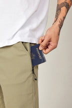 A person with a tattooed arm puts a navy blue passport into the zippered pocket of their olive green 686 Men's Everywhere® Ripstop Short - Relaxed Fit while wearing a white shirt.