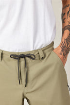 A person wearing 686 Men's Everywhere® Ripstop Short - Relaxed Fit in olive green and a white shirt has one hand in their pocket, revealing a detailed black dragon tattoo on their forearm.