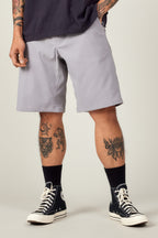 A person wears 686 Men's Everywhere® Ripstop Short - Relaxed Fit in light gray, a dark tee, black high-top sneakers, and black socks. Their tattooed arms and legs are visible as they stand against a plain light background.