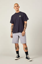 A tattooed person with short blond hair stands facing forward, wearing a black T-shirt, 686 Men's Everywhere® Ripstop Short - Relaxed Fit by 686, black socks, and black high-top sneakers against a plain background.