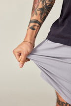 A tattooed person in a black shirt and 686 Men's Everywhere® Ripstop Short - Relaxed Fit stretches the durable fabric with their left hand, showcasing the impressive flexibility of these 686 shorts.