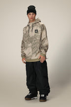 A person stands against a plain, light background wearing a black beanie, 686 Mens Bonded Fleece Pullover Hoody by 686 in beige camouflage with a logo patch, black cargo pants, and black boots.