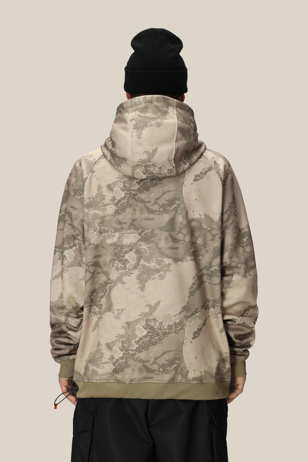 A person wearing the 686 Mens Bonded Fleece Pullover Hoody in a beige and olive green camo pattern, paired with a black beanie, stands with their back to the camera against a plain light tan background.