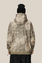 A person wearing the 686 Mens Bonded Fleece Pullover Hoody in a beige and olive green camo pattern, paired with a black beanie, stands with their back to the camera against a plain light tan background.
