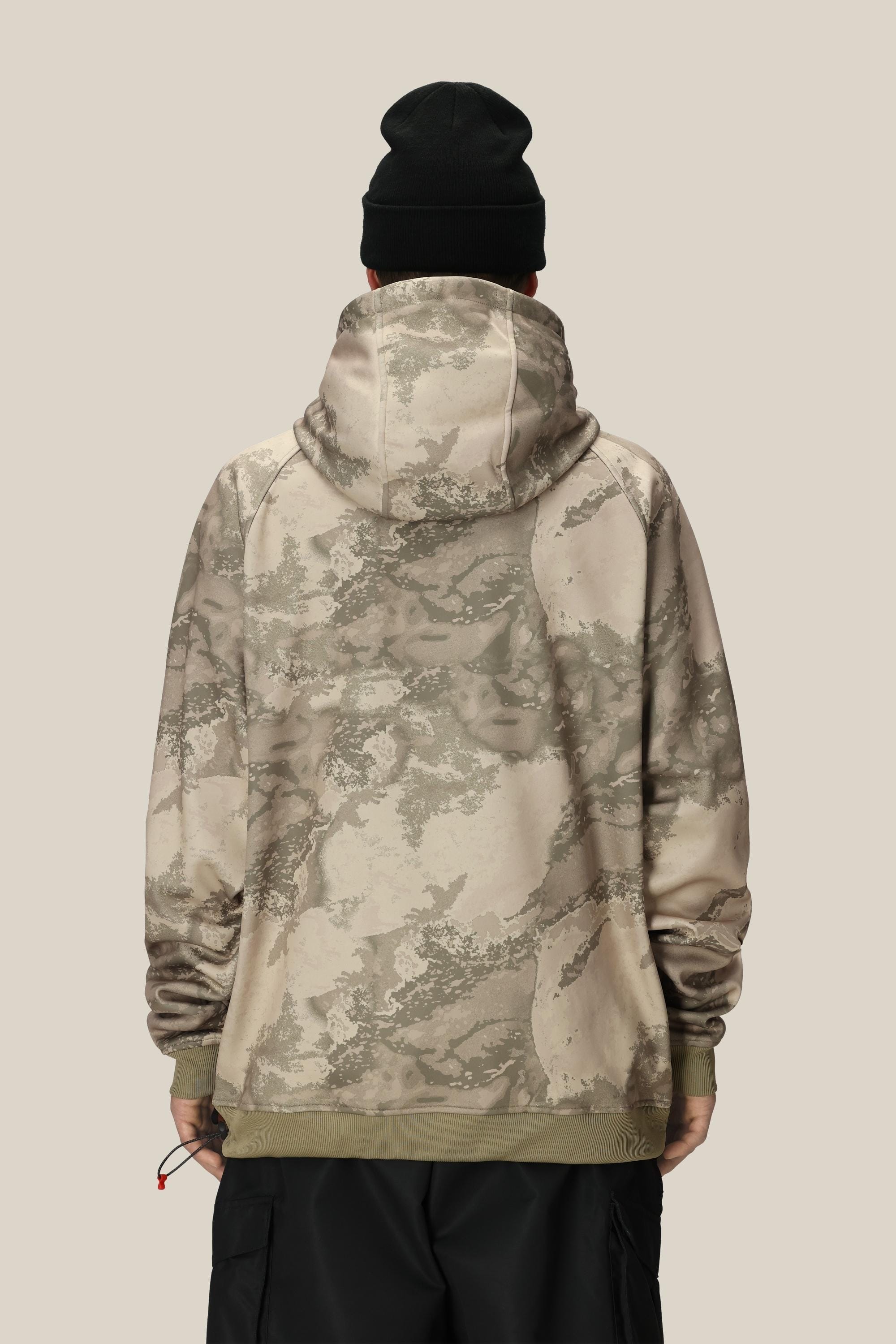 A person wearing the 686 Mens Bonded Fleece Pullover Hoody in a beige and olive green camo pattern, paired with a black beanie, stands with their back to the camera against a plain light tan background.