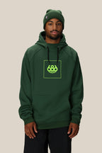 A man wears the 686 Mens Bonded Fleece Pullover Hoody featuring a neon green 686 logo and pairs it with a matching green beanie, standing against a plain beige background.