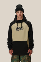 A young man wears the 686 Mens Bonded Fleece Pullover Hoody in tan and black, featuring a stylized 666 logo, paired with a black beanie and camouflage pants, standing against a plain beige background.