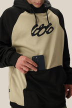 A person wearing the 686 Mens Bonded Fleece Pullover Hoody, featuring a two-tone beige and black design with cozy fleece lining, places a black smartphone into the front kangaroo pocket. The brand “686” is visible on the hoodie.