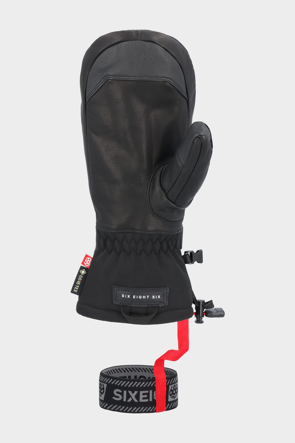 The 686 Men's GORE-TEX Leather Linear™ Mitt features black insulation, a leather palm, fabric cuff, adjustable wrist strap with red pull tab, and 686 branding on the labels and elastic band below.