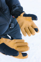 Wearing a dark jacket and pants, a person stands on snow, displaying both hands in 686 Men's GORE-TEX Leather Linear™ Gloves with leather palms for grip and waterproof protection.