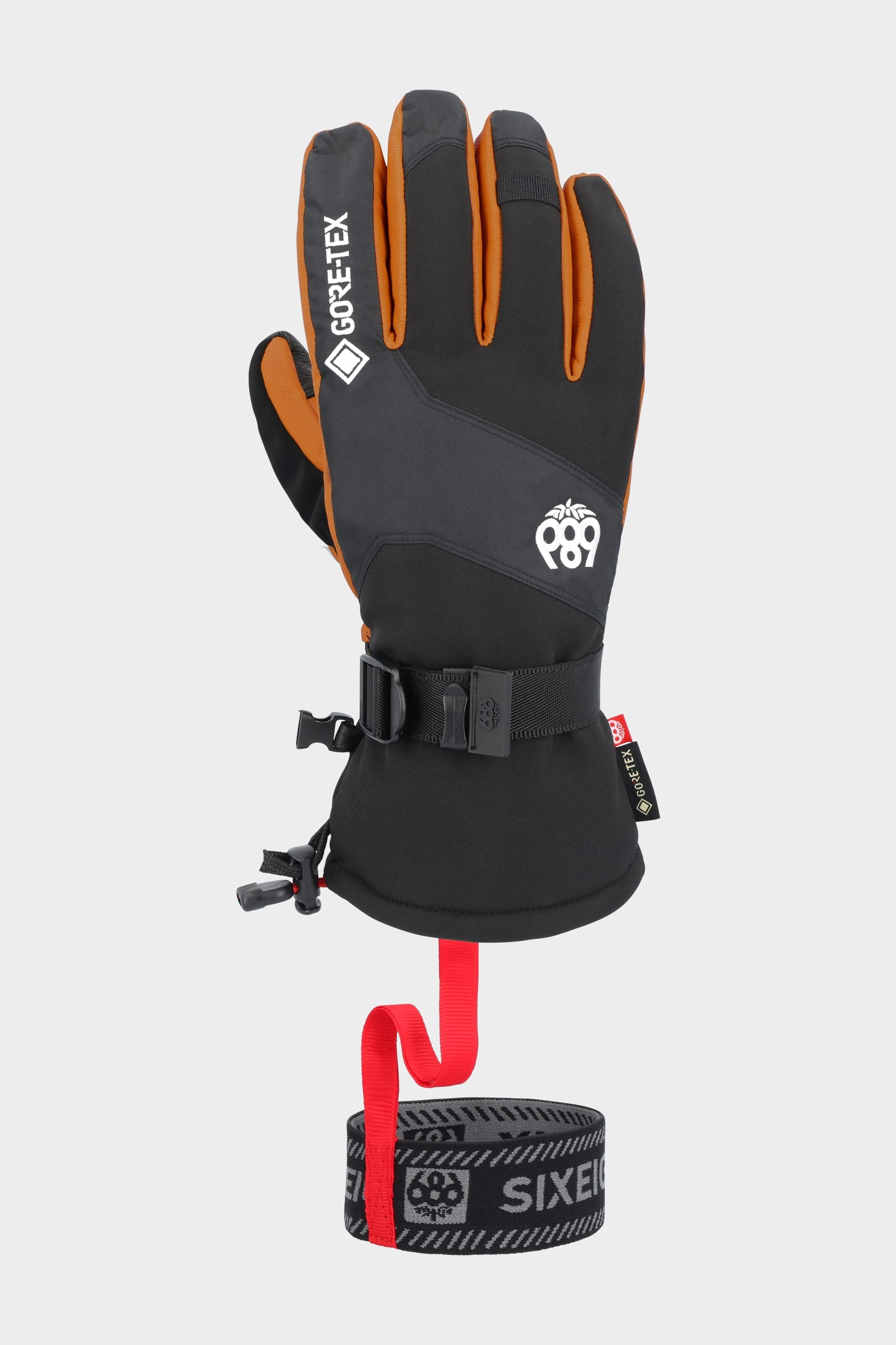The 686 Men's GORE-TEX Leather Linear™ Glove, shown upright on a red-based stand, displays its black and orange palm with reinforced leather areas, waterproof GORE-TEX protection, and an adjustable wrist strap.