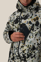 A person wearing the 686 Men's Hydra™ Thermagraph® Jacket with a hood and body-mapped lining is putting a black smartphone into its zippered chest pocket against a plain, light-colored background.