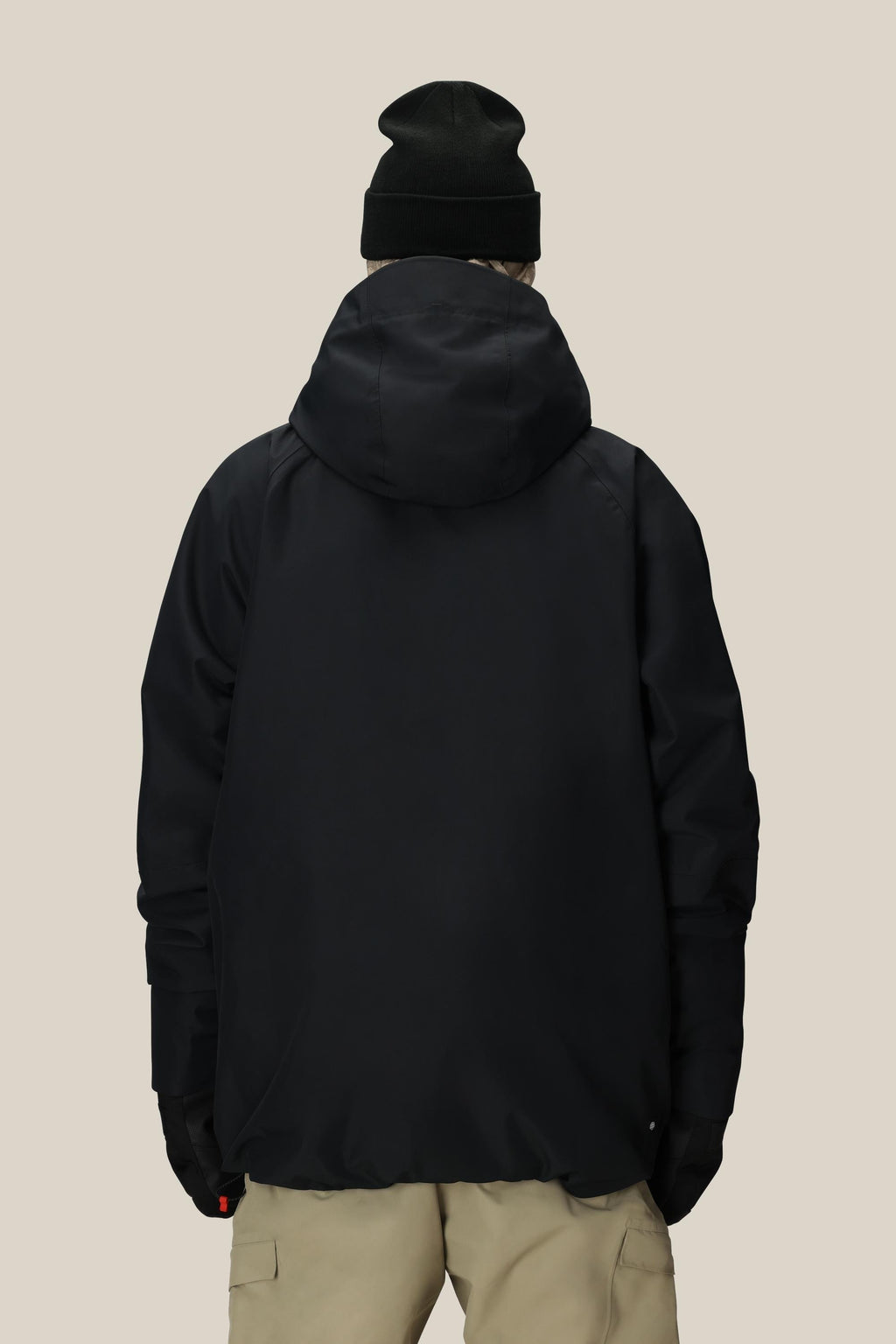 A person is shown from the back against a beige background wearing the 686 Men's Hydra™ Thermagraph® Jacket, black gloves, a black beanie, and light-colored pants.
