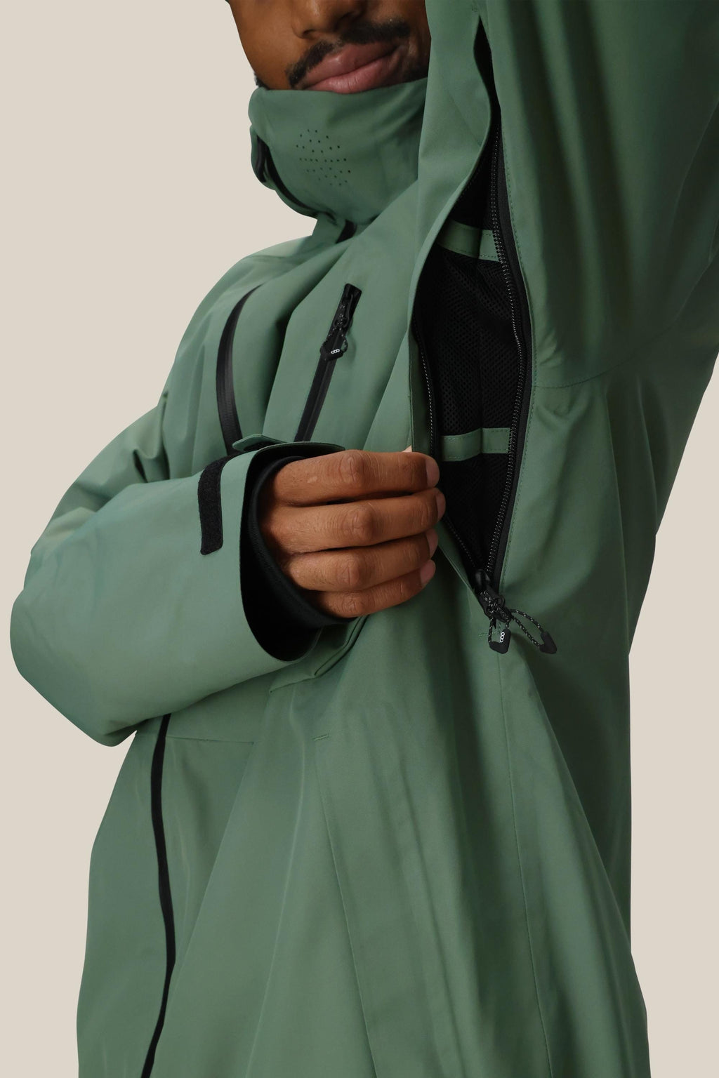 A person wears the 686 Men's Hydra™ Thermagraph® Jacket in green, unzipping an underarm vent to reveal body-mapped black mesh lining. Only their lower face and torso are visible against a plain, light background. Brand: 686.