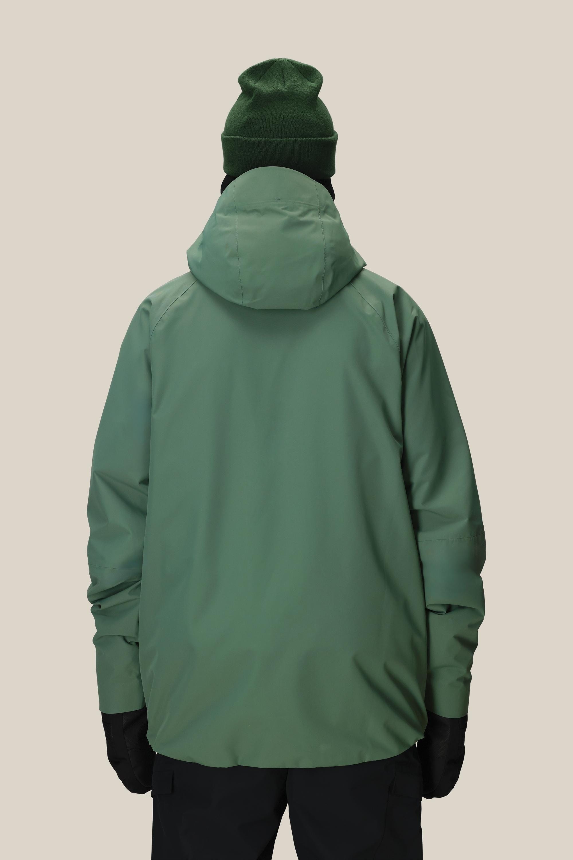 A person wearing the 686 Men's Hydra™ Thermagraph® Jacket by 686, paired with a dark green beanie, black gloves, and black pants, is shown from the back against a plain beige background.