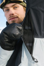 A person in the 686 Men's Hydra™ Thermagraph® Jacket with body-mapped lining and black mittens unzips a mesh sleeve vent outdoors, their face partially visible in a cold or snowy setting.