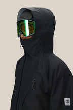 A person in the 686 Men's Hydra™ Thermagraph® Jacket, featuring a high collar, paired with green reflective ski goggles and a helmet, shown from the side against a plain beige background.