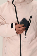 A person wearing the 686 Men's Hydra™ Thermagraph® Jacket in light pink zips a black smartphone into the chest pocket. This best seller from 686 features black zippers, body-mapped lining, and a Velcro sleeve strap.