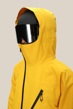 A man wears the 686 Men’s Hydra™ Thermagraph® Jacket in bright yellow, featuring a visible zipper and chest loop, paired with oversized black ski goggles and a black helmet, facing left against a plain light background.