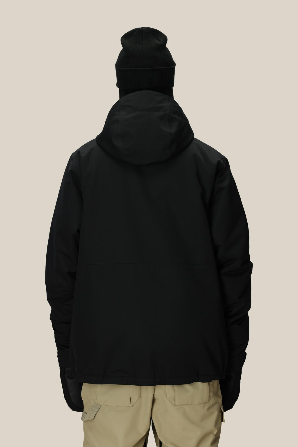 A person is shown from the back against a plain light background wearing the 686 Men's Foundation™ Insulated Jacket, a black hooded polyester jacket by 686, paired with a black beanie, black gloves, and beige pants.