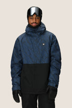 A person in a 686 Men's Foundation™ Insulated Jacket by 686, black gloves, ski goggles, and a black beanie stands against a plain light background.