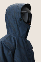 A person wearing a 686 Men's Foundation™ Insulated Jacket in dark blue, paired with black ski goggles and a black helmet, is shown from the side against a plain light background.