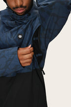 A person wearing the 686 Men's Foundation™ Insulated Jacket in a blue and black pattern unzips a side vent under the arm, revealing black mesh lining. Only their face and upper body are partially visible.