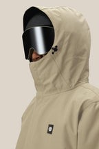 A man in a beige 686 Men's Foundation™ Insulated Jacket with a high collar, large black ski goggles, and a black helmet is shown from the side against a plain background.
