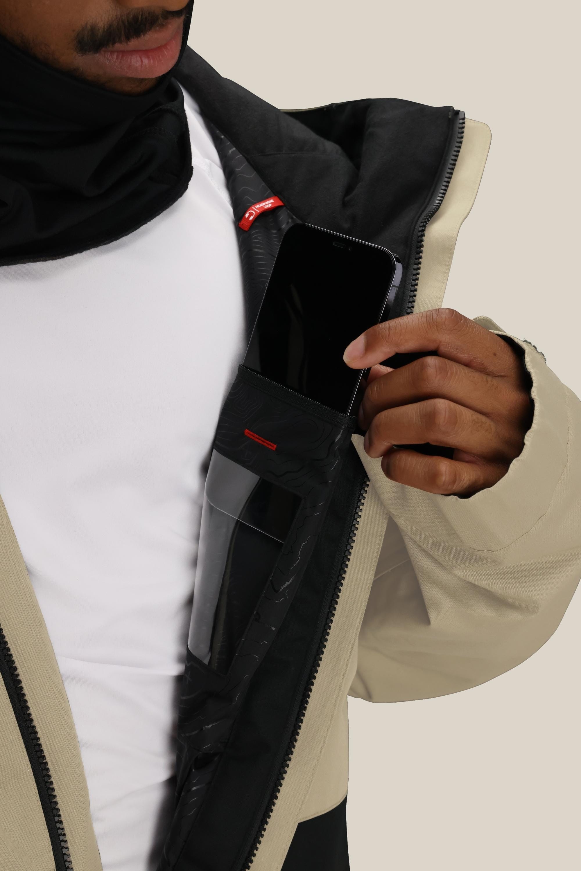 A man wearing the 686 Men's Foundation™ Insulated Jacket slips a smartphone into its inner zippered chest pocket, showing off the phone’s screen and the jacket’s soft lining.