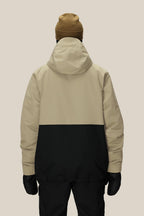 A person wearing a tan and black 686 Men's Foundation™ Insulated Jacket, black pants, black gloves, and a brown beanie stands facing away against a plain light background.