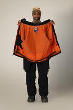 A person in black pants, boots, and a tan beanie holds open the 686 Dojo® Jacket by 686, showing its bright orange lining to the camera.